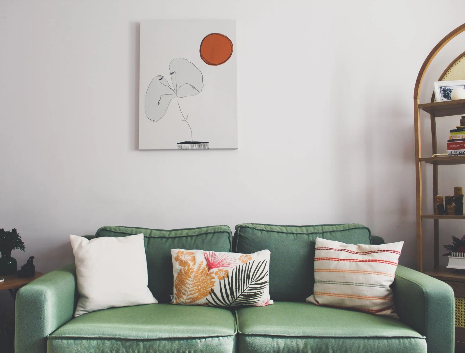A small vertical artwork centered above a green sofa, showing the relationship between frame width and seating width.