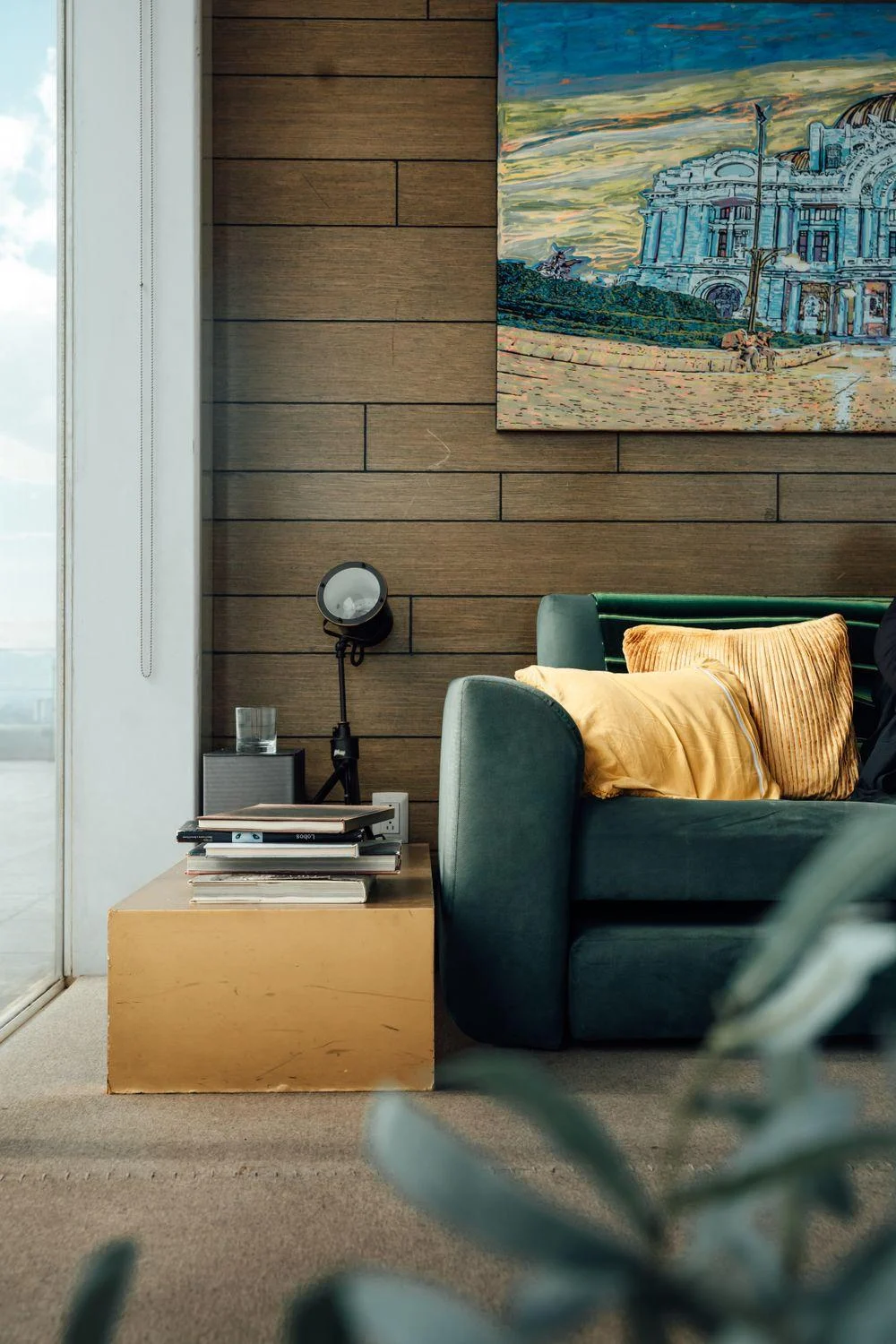 An artwork and green sofa set against a wall of warm wood planks.