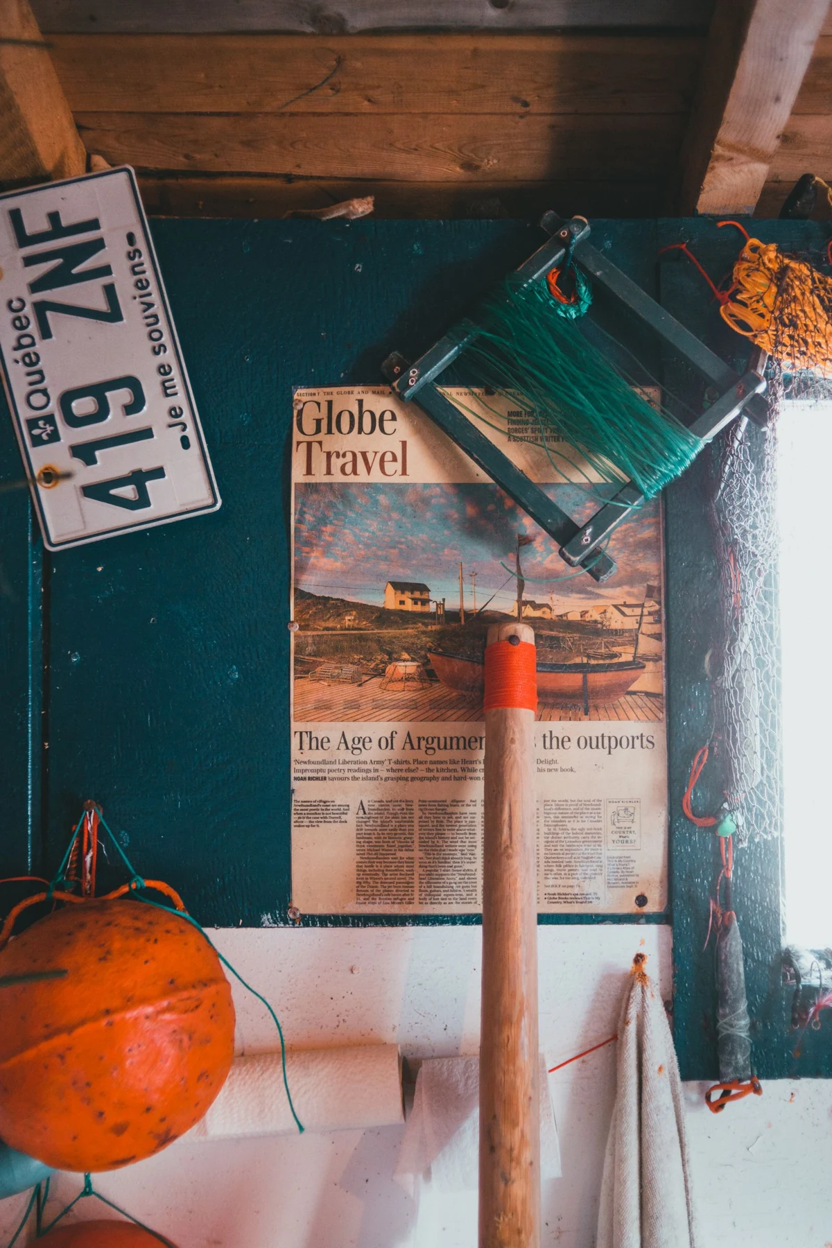 A vintage travel poster on a teal wall beside a wooden pole and travel objects.