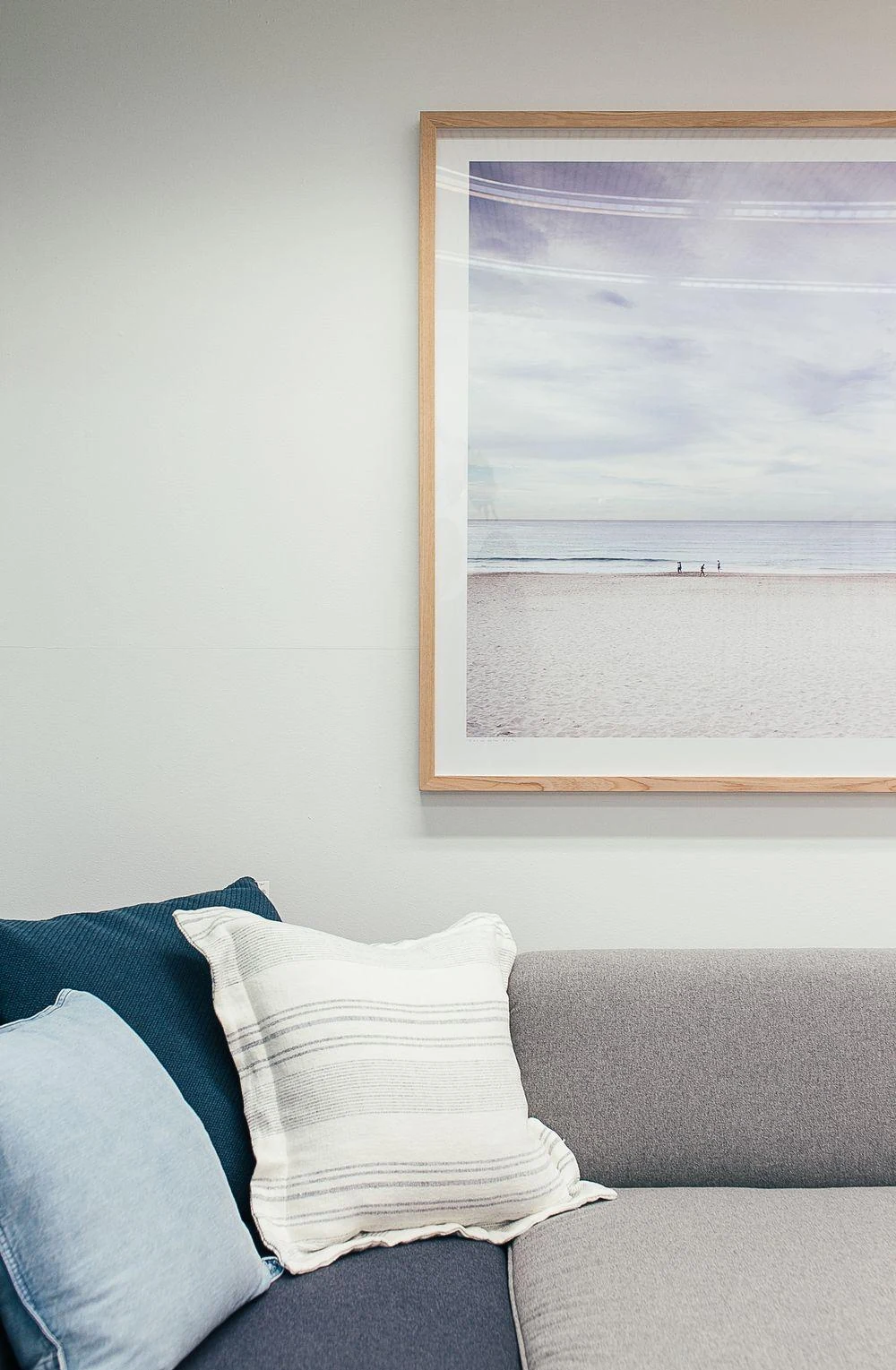A pale coastal print and neutral sofa illustrate a restrained palette for an art gift.