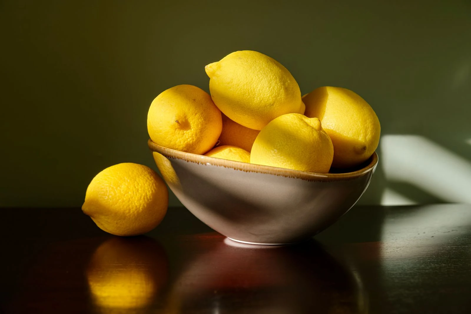 Sunlit yellow lemons in a ceramic bowl, illustrating a food still life for a cooking enthusiast.